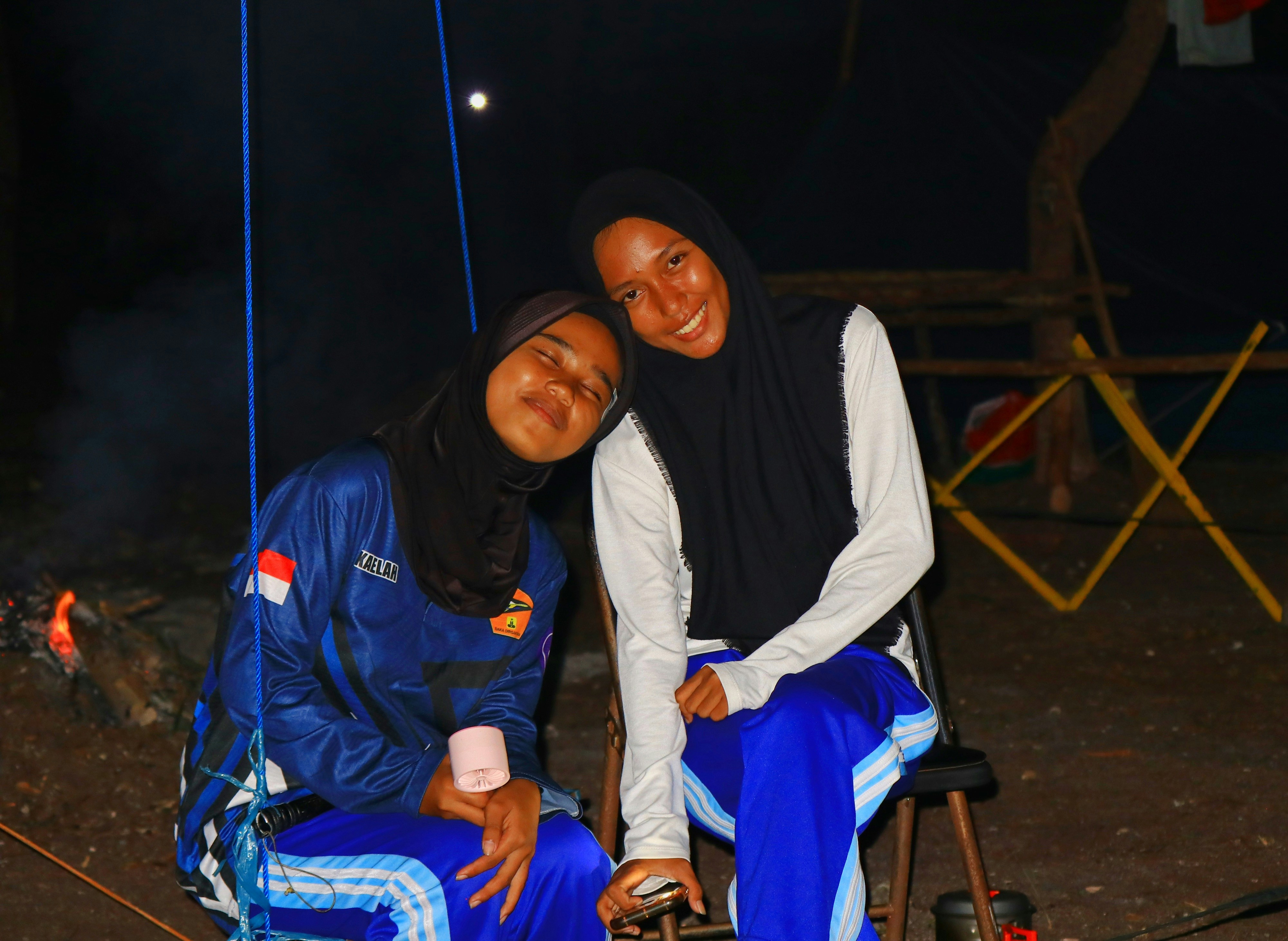Two smiling young women in hijabs at night.