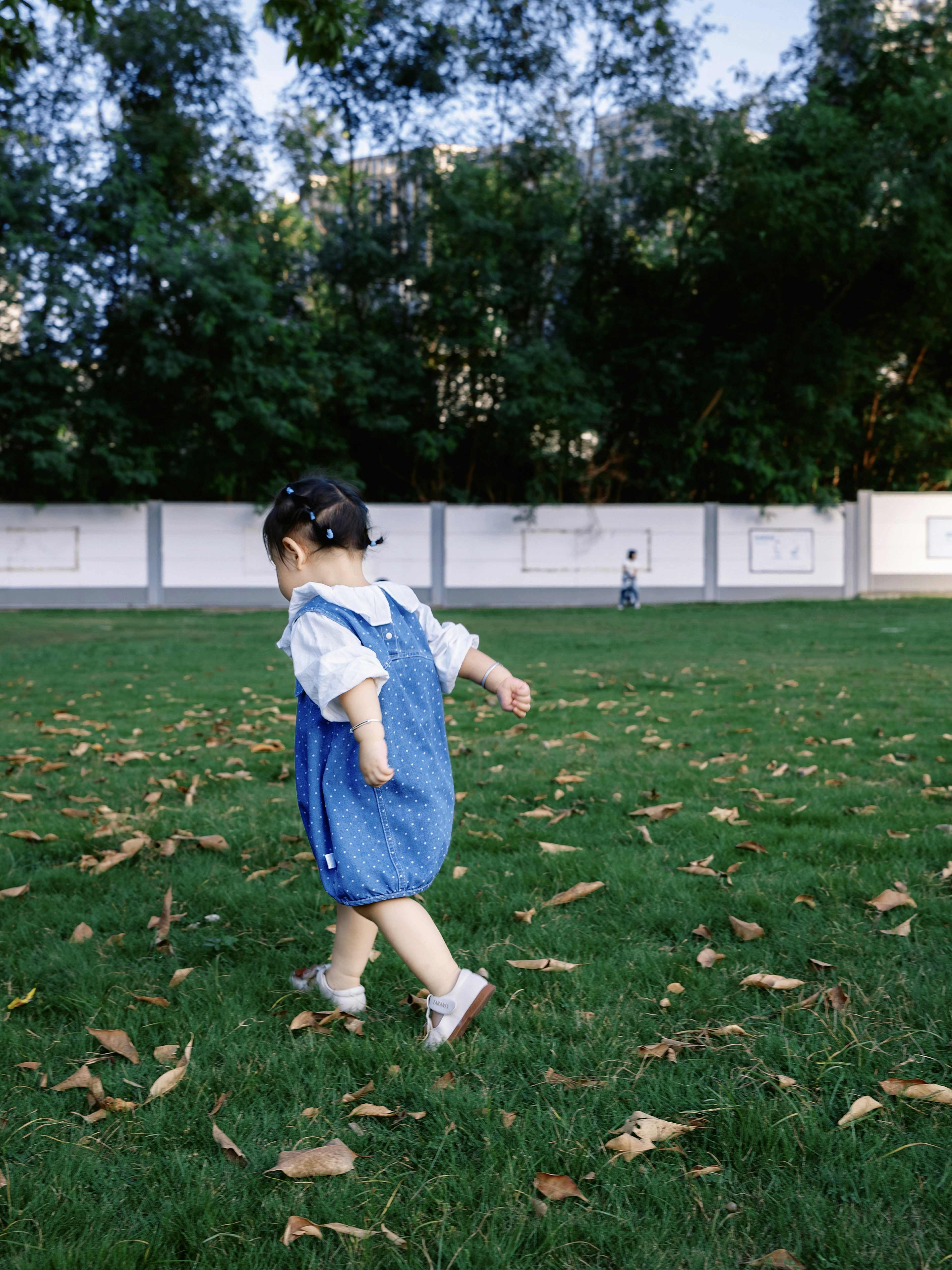 A young child in a blue outfit walks on grass.