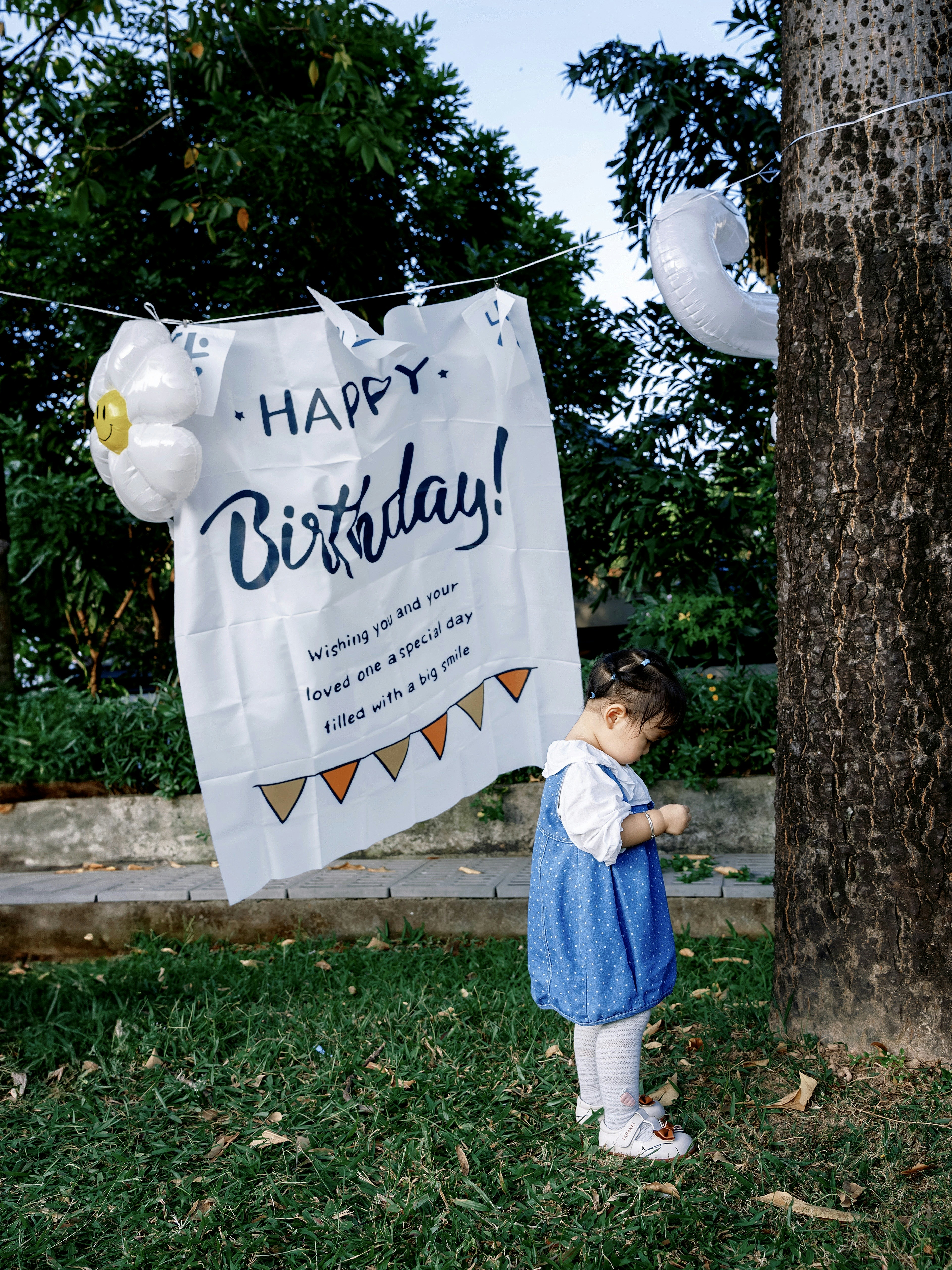 Girl in blue dress near birthday banner with balloons