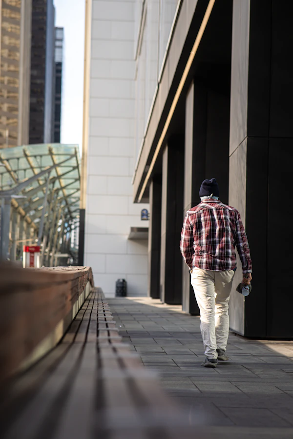 Man in unbuttoned plaid overshirt walking on city sidewalk in mild weather