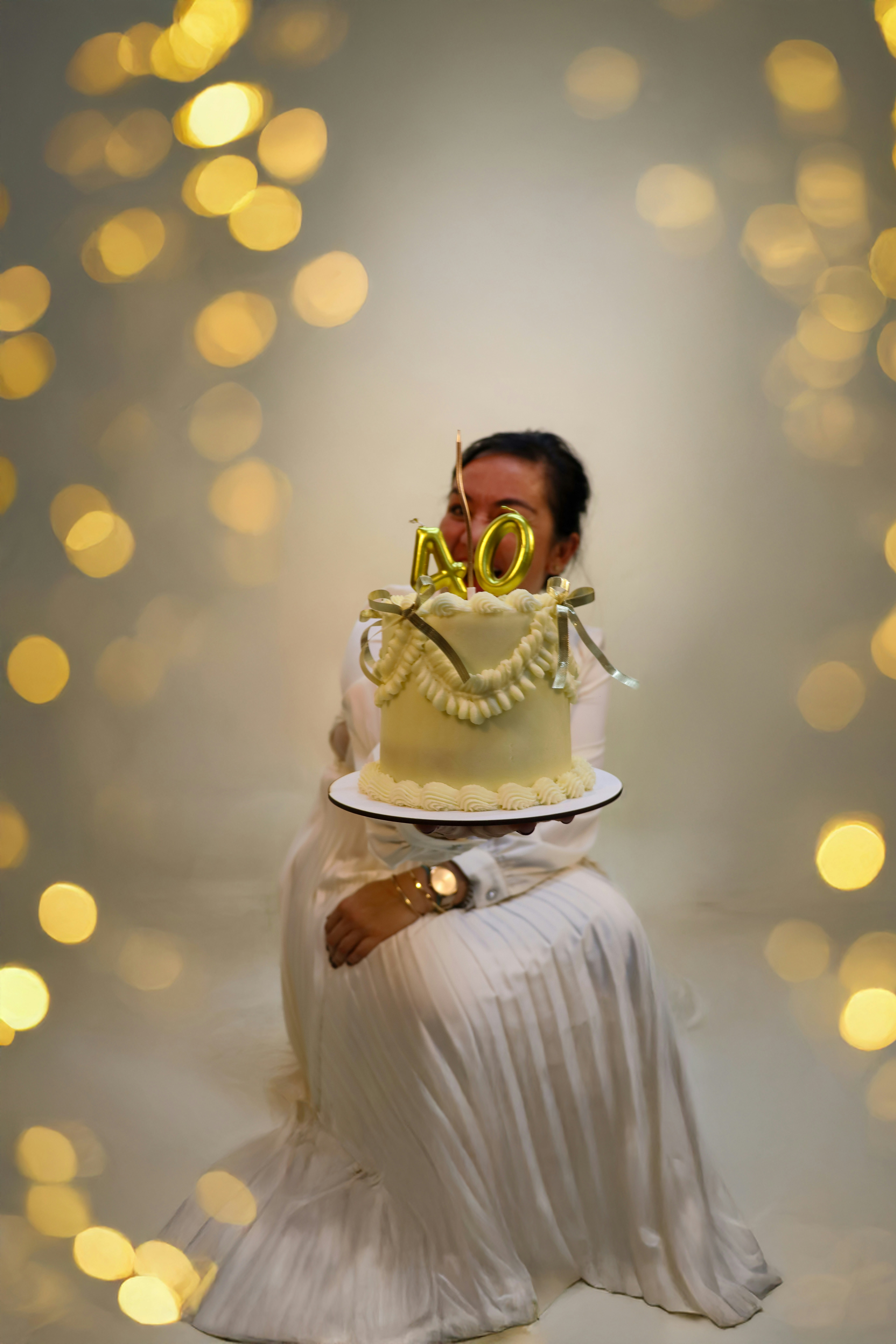 Frau hält einen dekorierten Kuchen mit goldenen Zahlenballons.