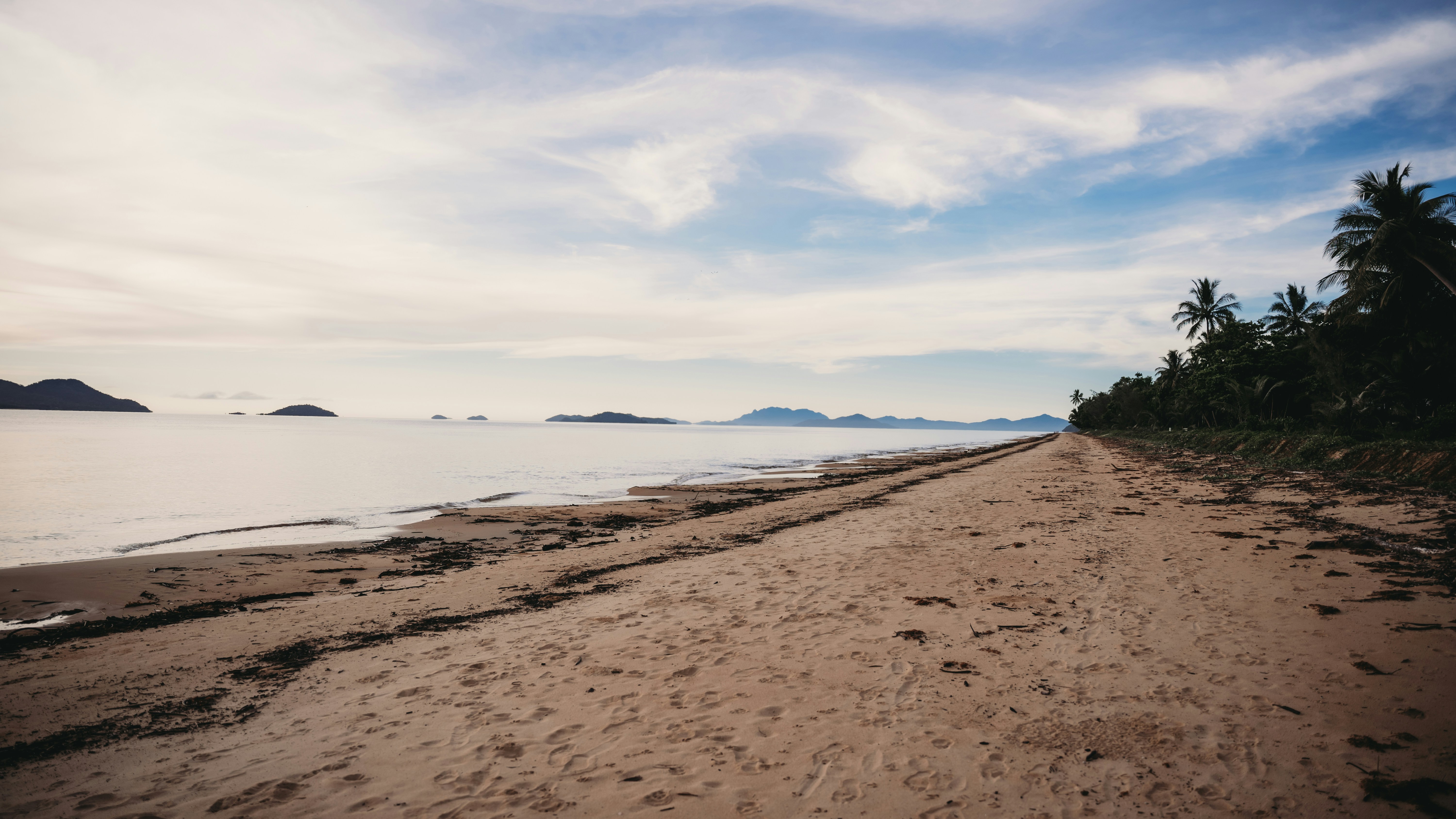 Sandy beach with ocean and distant islands under clouds