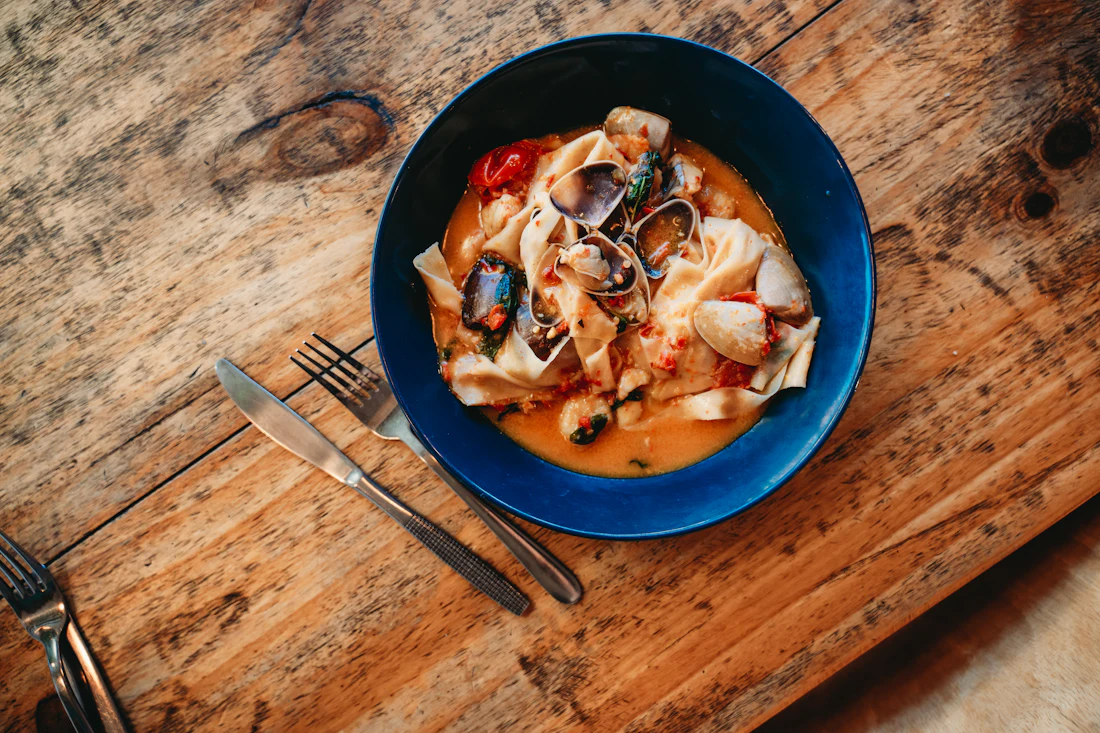 Pappardelle con frutti di mare in un piatto fondo blu visto dall'alto