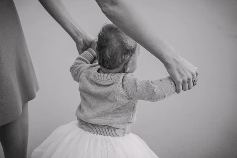 Adults holding a young child's hands as she learns to walk