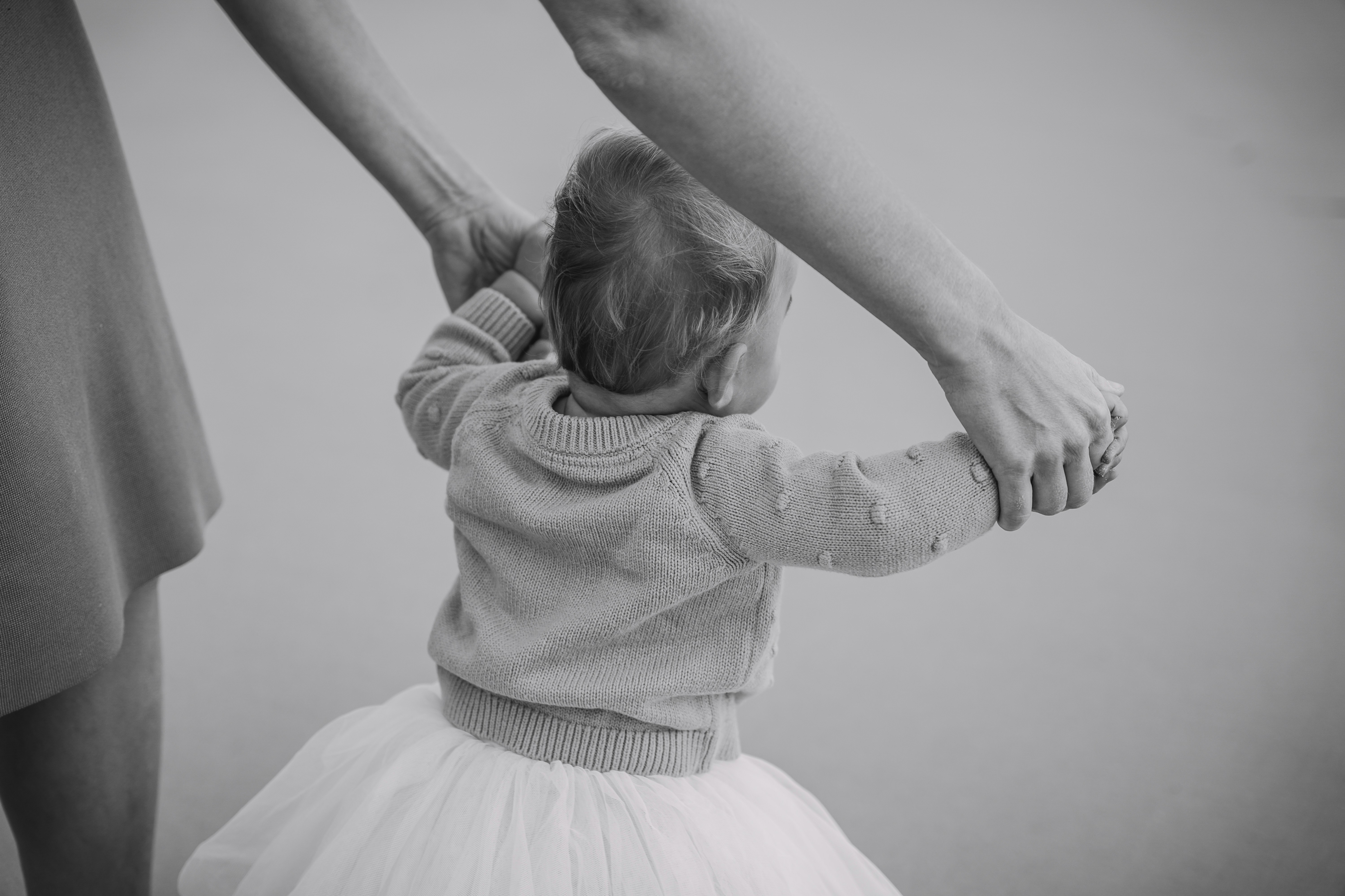 Adults holding a baby's hands, helping her walk.