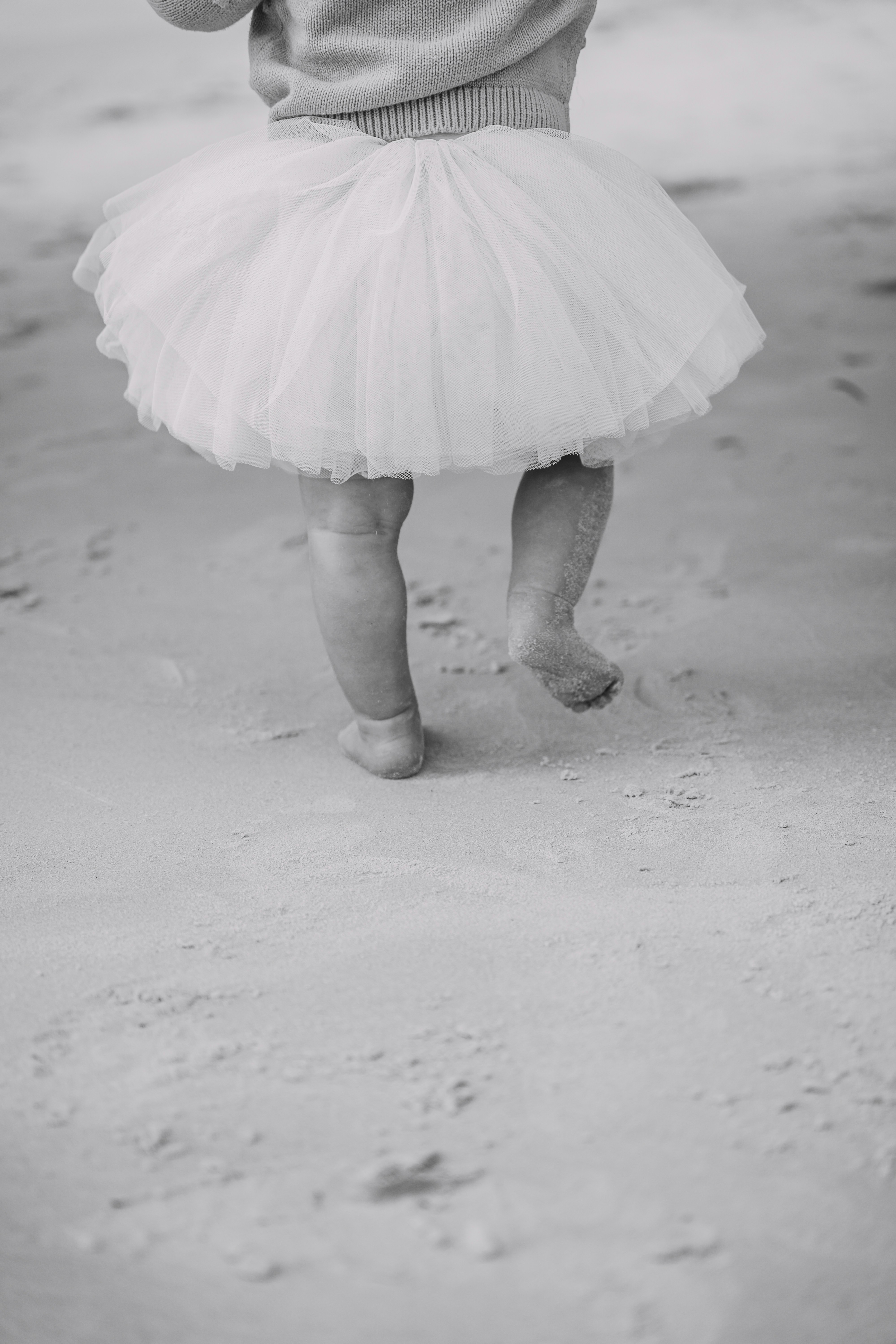 A child in a tutu walks on the sand.
