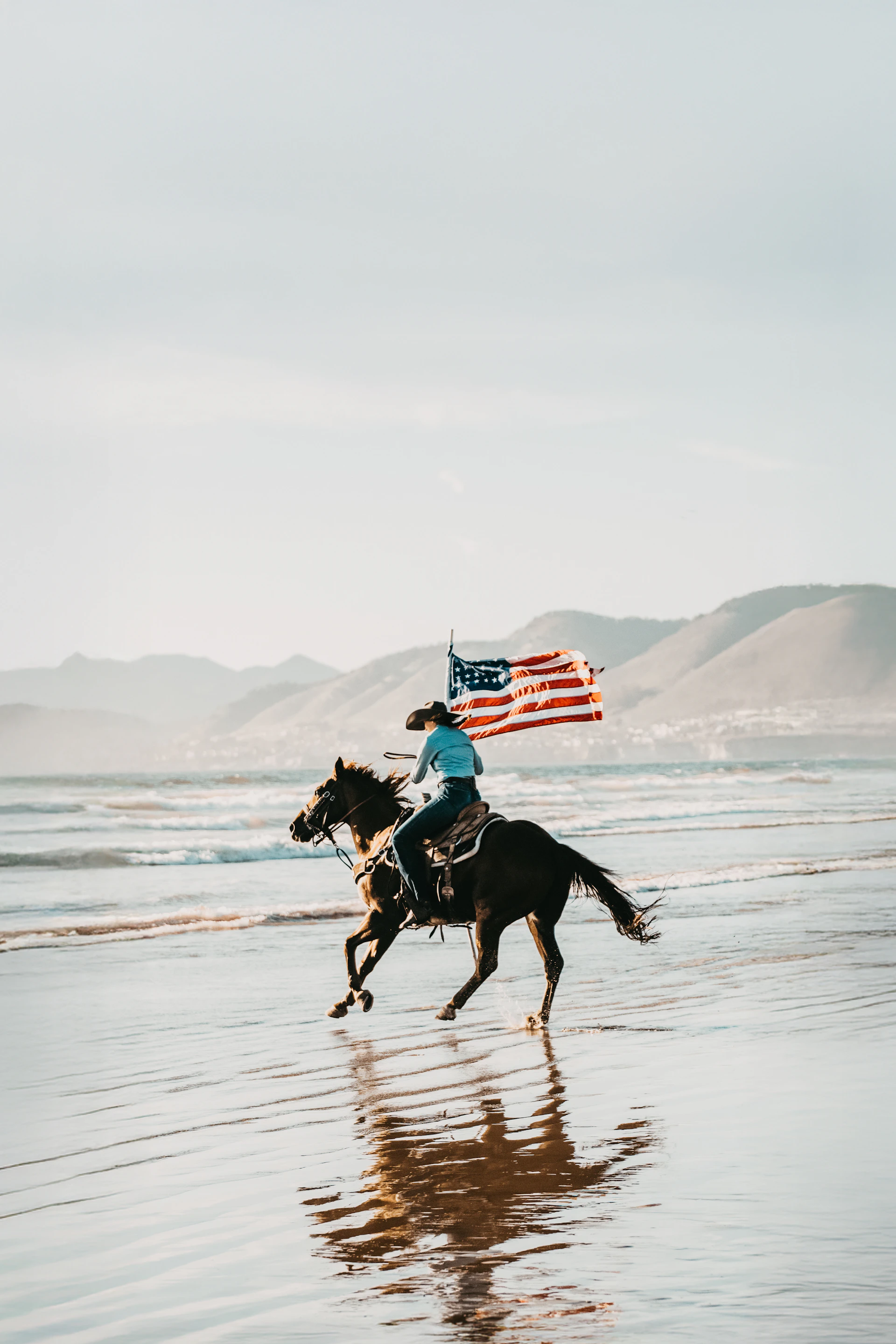 Cowgirl rides horse with american flag on beach