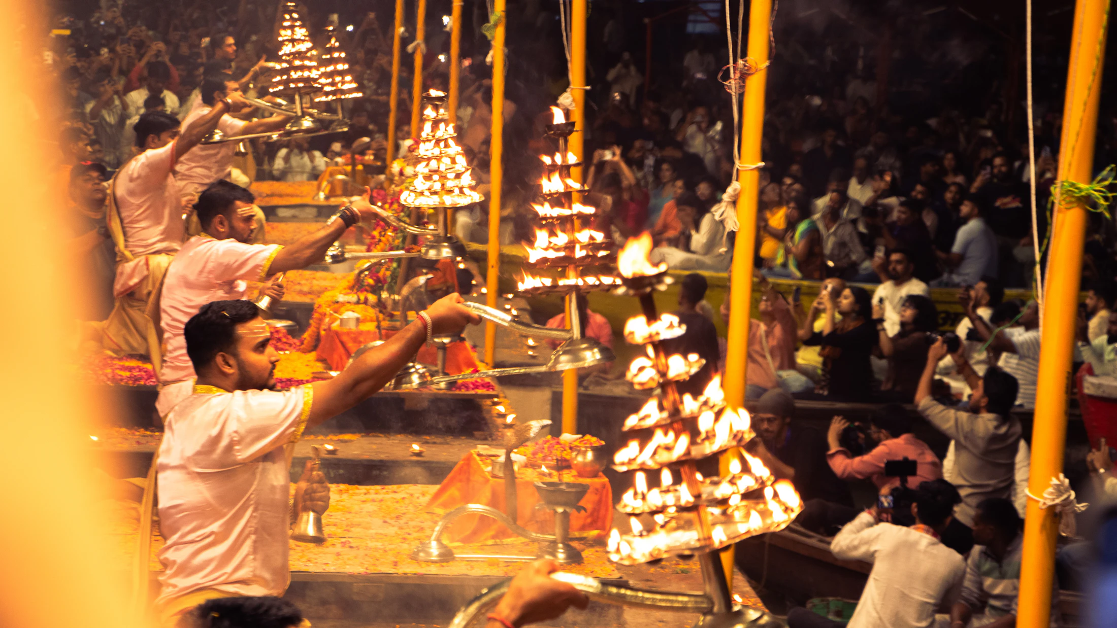 Priests holding tiered brass lamps during the evening aarti, crowds behind