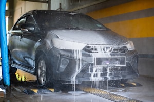 A dark car being washed with foam and water.