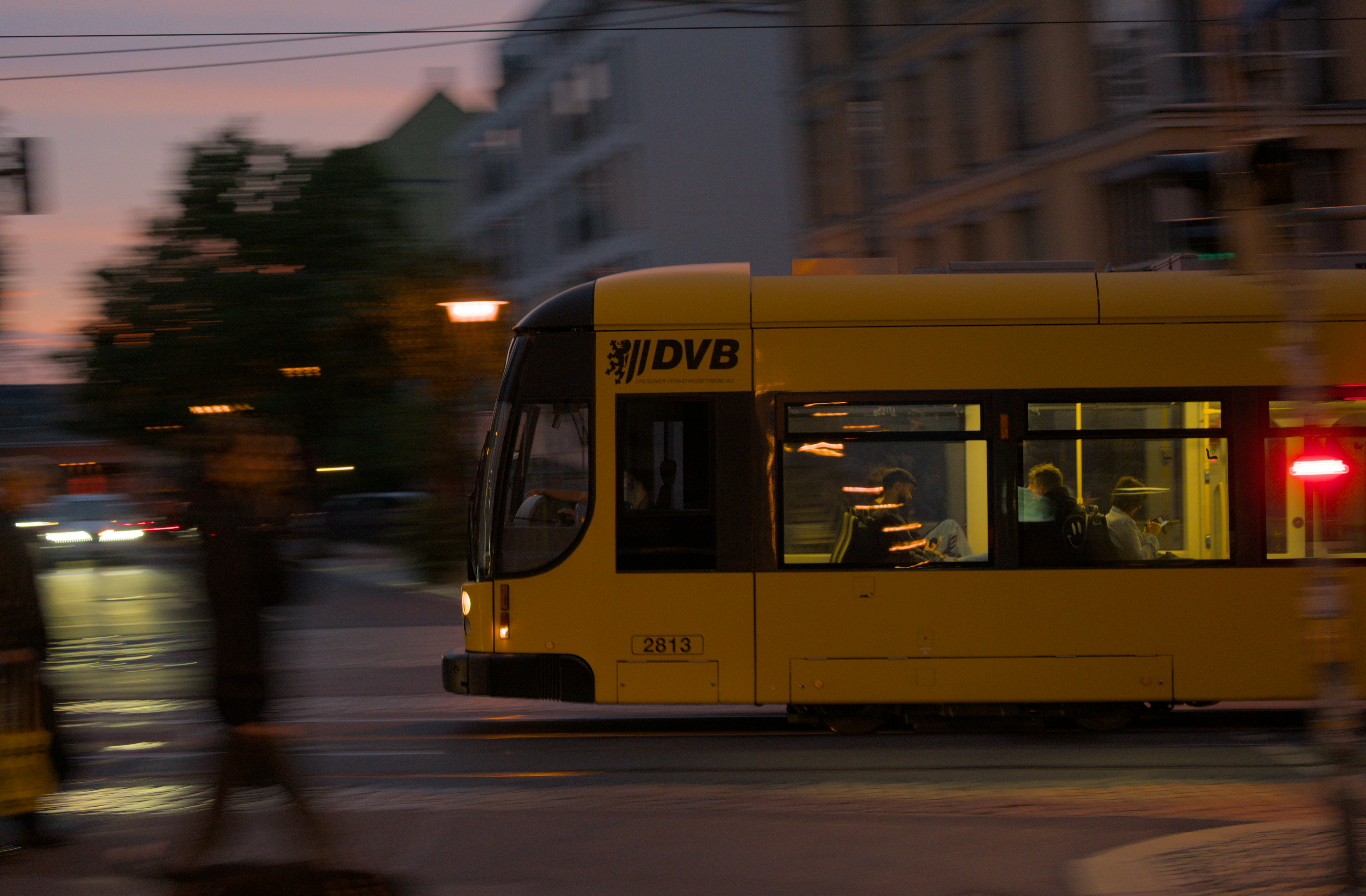 Yellow tram moving through city street at dusk