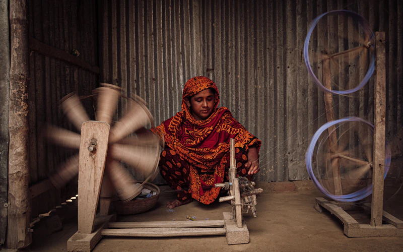 An artisan spinning cotton thread by hand on a traditional wooden wheel