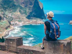 Man with backpack overlooks coastal village and ocean.