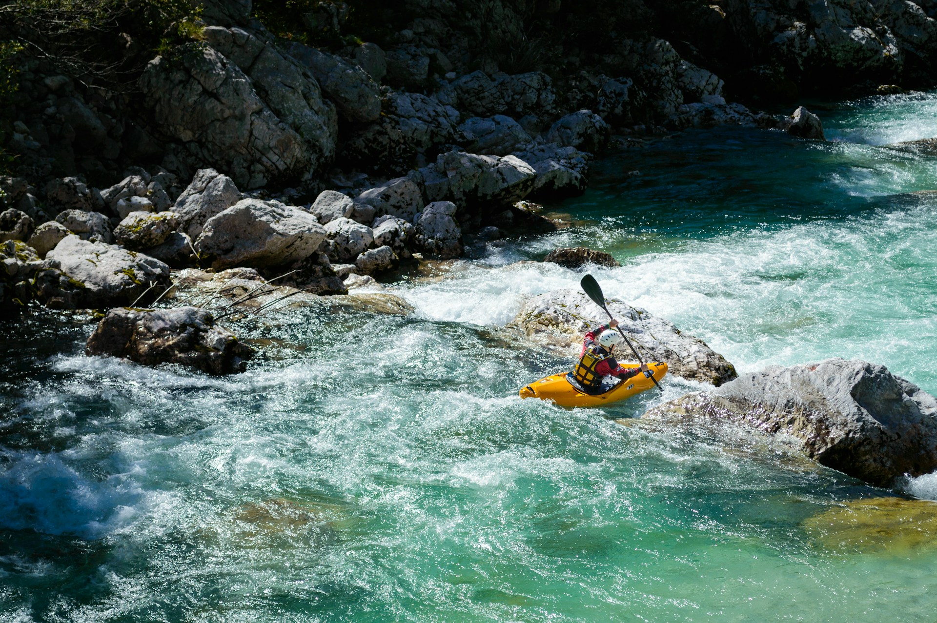 A person kayaks down a rocky, turquoise river.