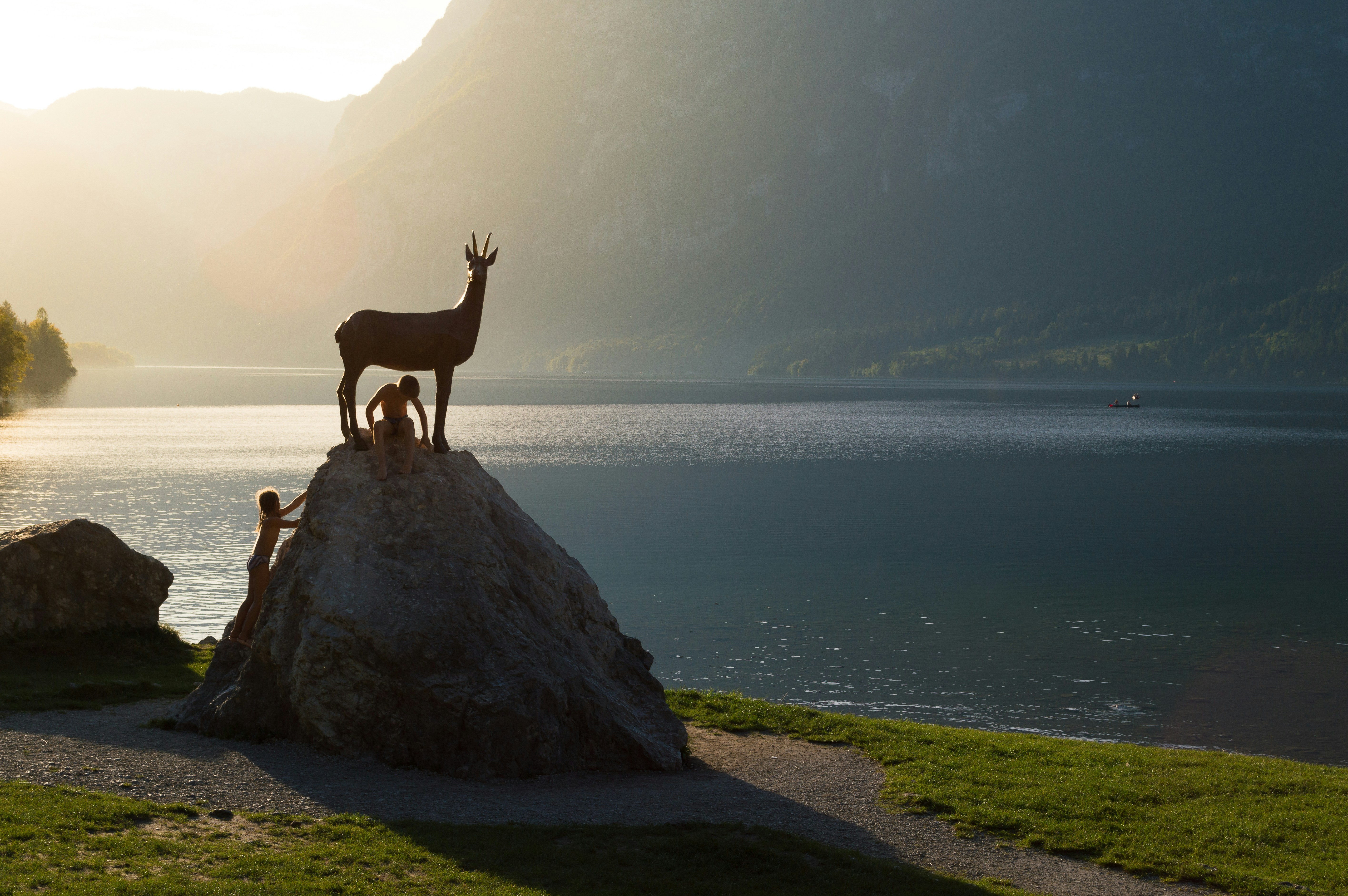 Deer statue on rock overlooking serene lake at sunset.