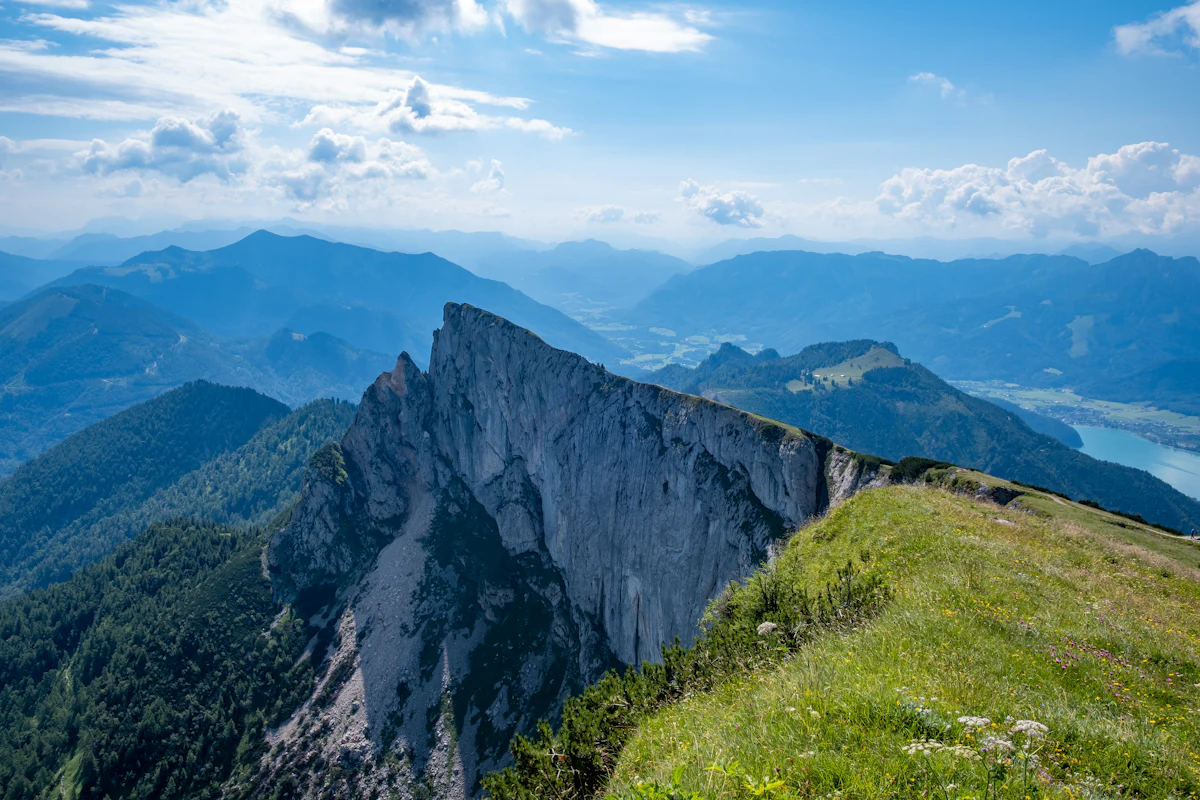A sheer limestone cliff on the Schafberg, with grassy slopes and blue ridges behind