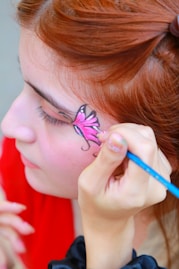 Face painting of a pink butterfly on a girl's cheek