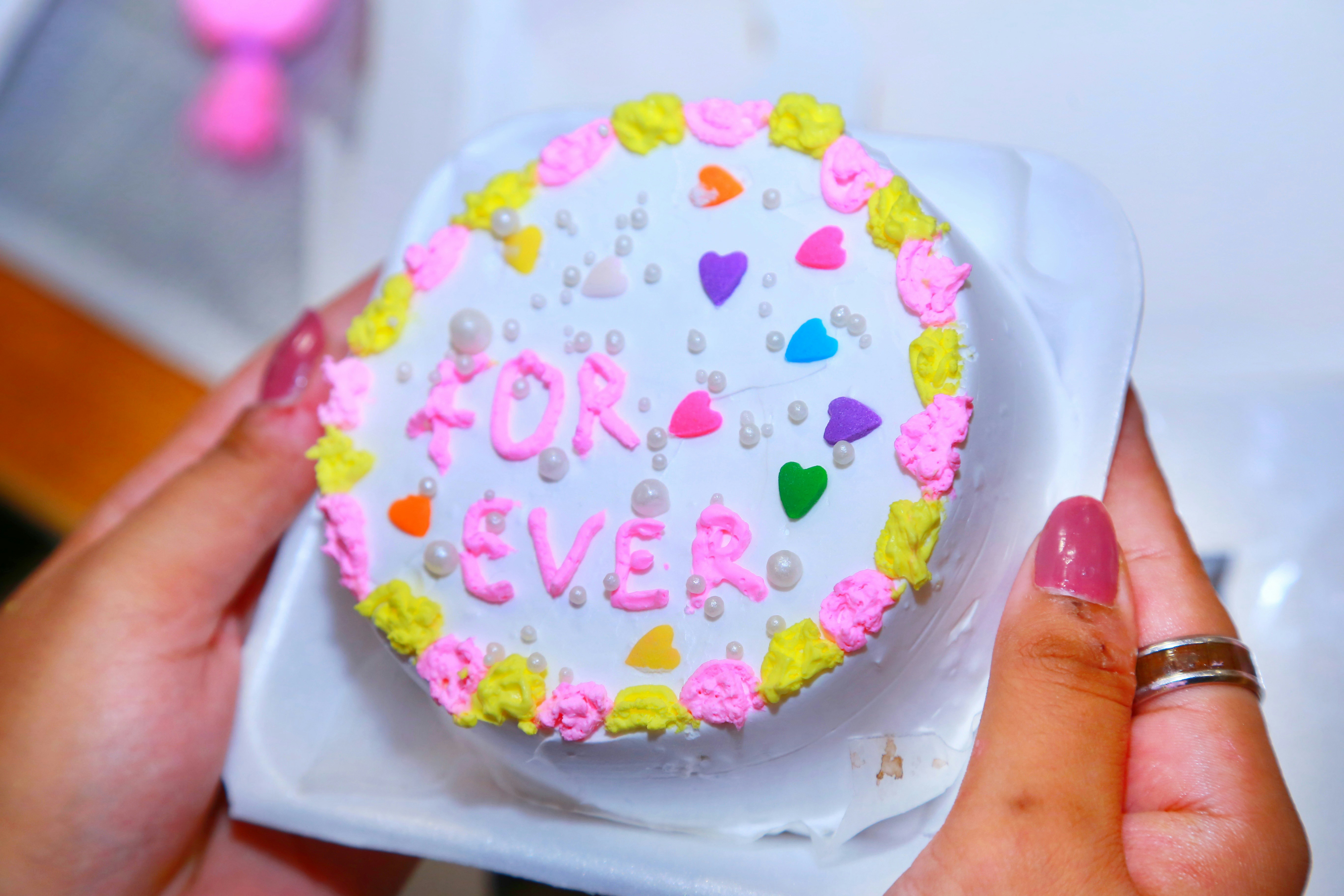 Mãos segurando um pequeno bolo decorado com corações.