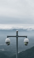 Two surveillance cameras on a pole with mountains behind