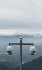 Two surveillance cameras on a pole with mountains behind