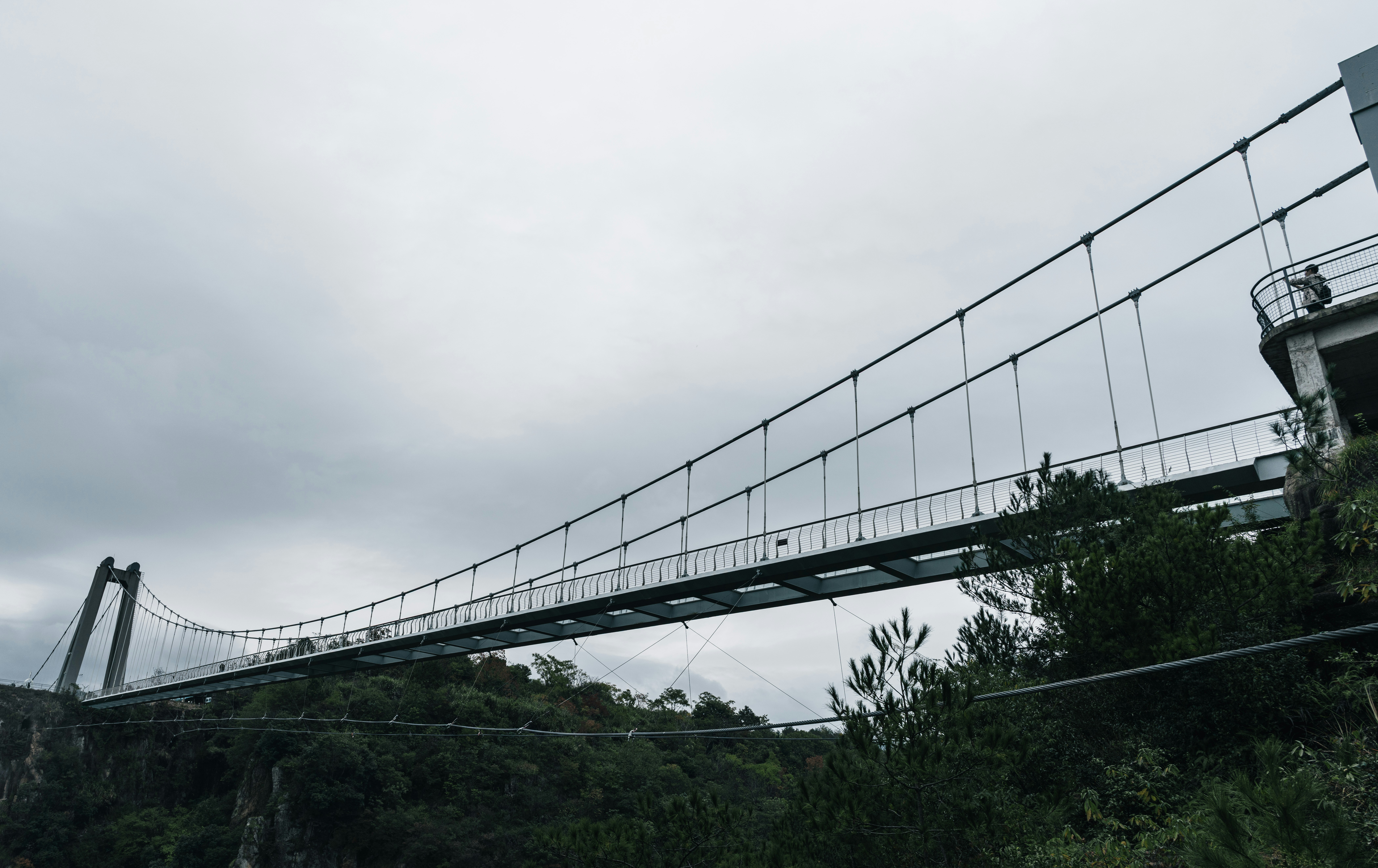 A long suspension bridge spans a cloudy sky.
