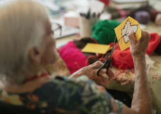 Elderly woman crafts autumn leaf decoration with scissors.