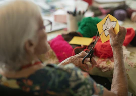 Elderly woman crafts autumn leaf decoration with scissors.