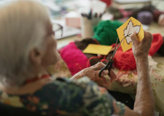 Elderly woman crafts autumn leaf decoration with scissors.