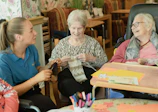 Caregiver assists two elderly women knitting