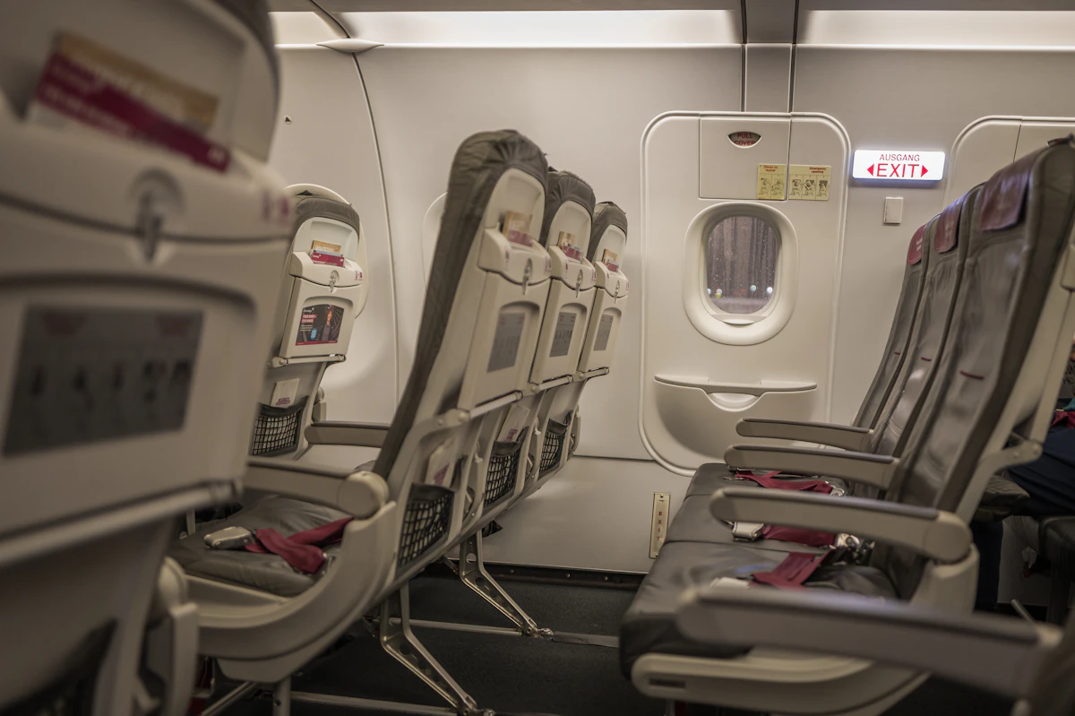 An empty airplane cabin with rows of burgundy seats and a window framing a blurred city view
