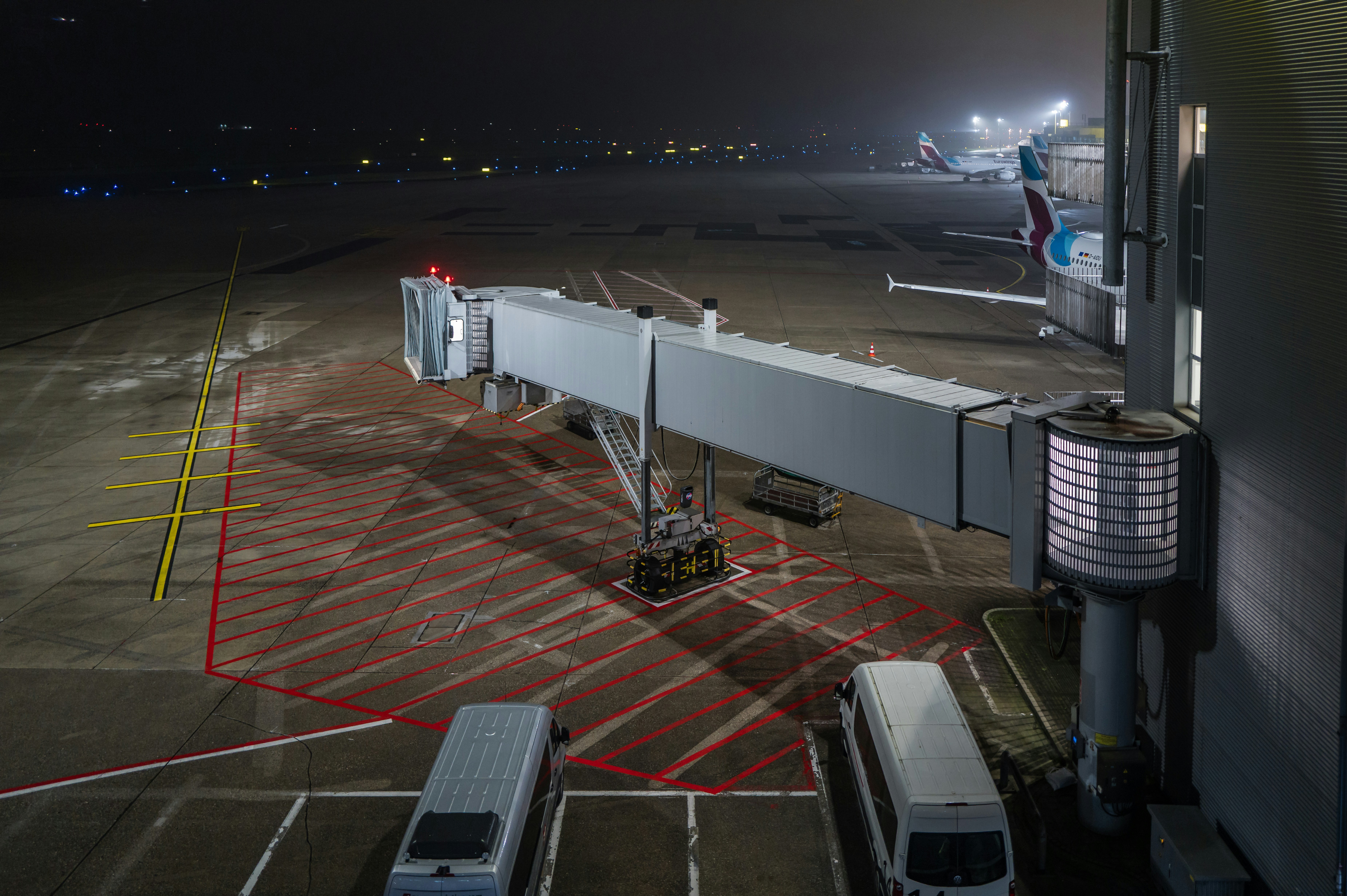 Airport jet bridge at night with planes and vehicles.