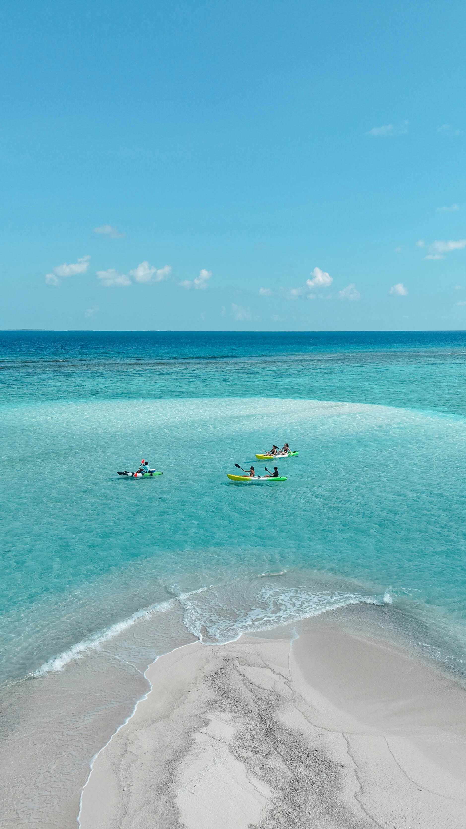 People kayaking in turquoise water near a sandy beach.