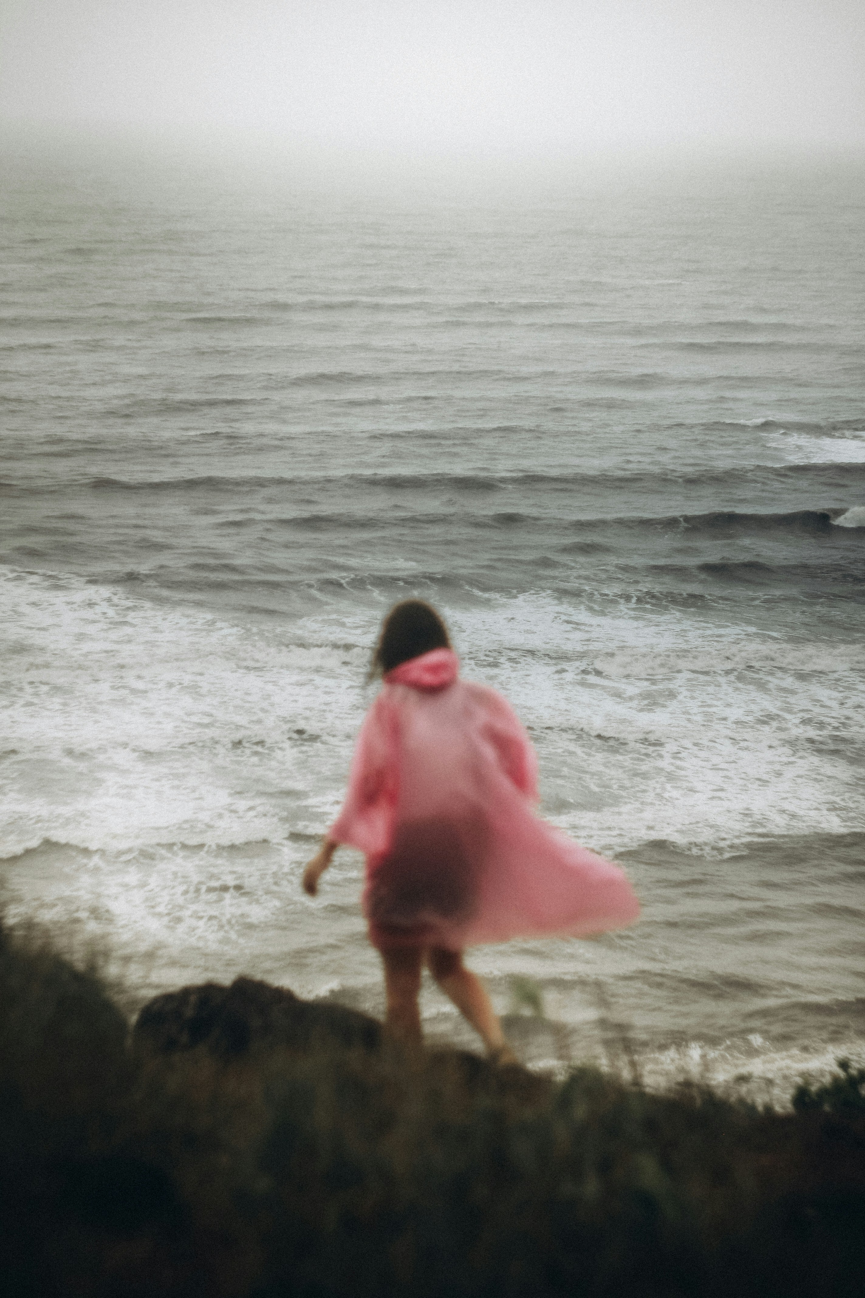 Person in pink raincoat facing the ocean waves