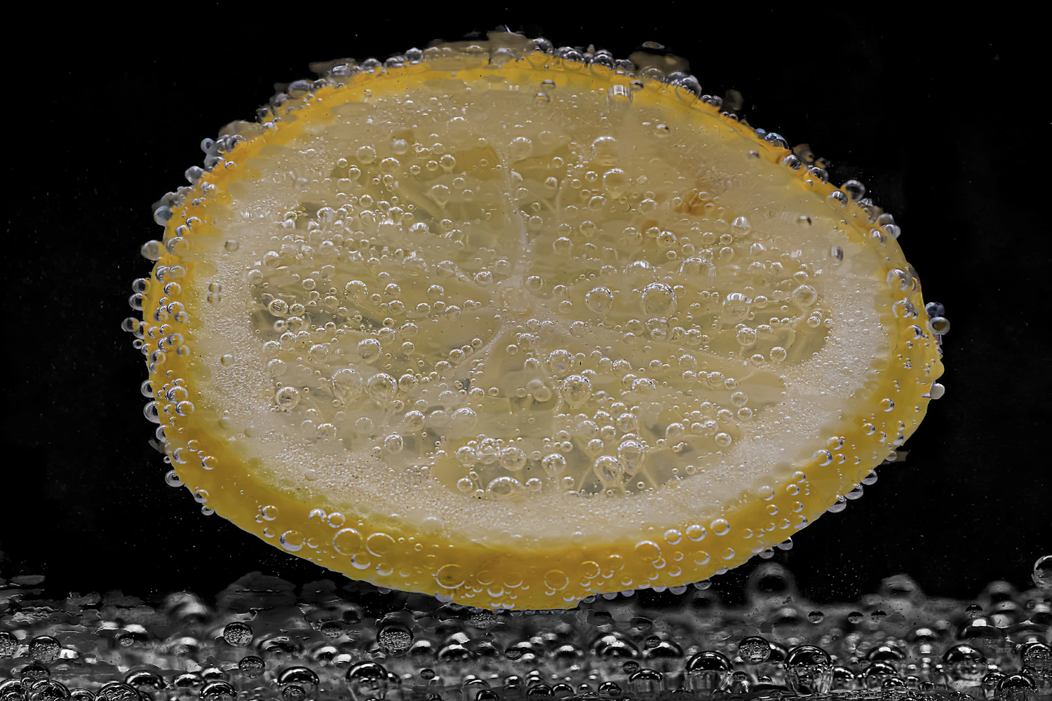 A slice of lemon suspended in sparkling water, bubbles clinging to it, on black
