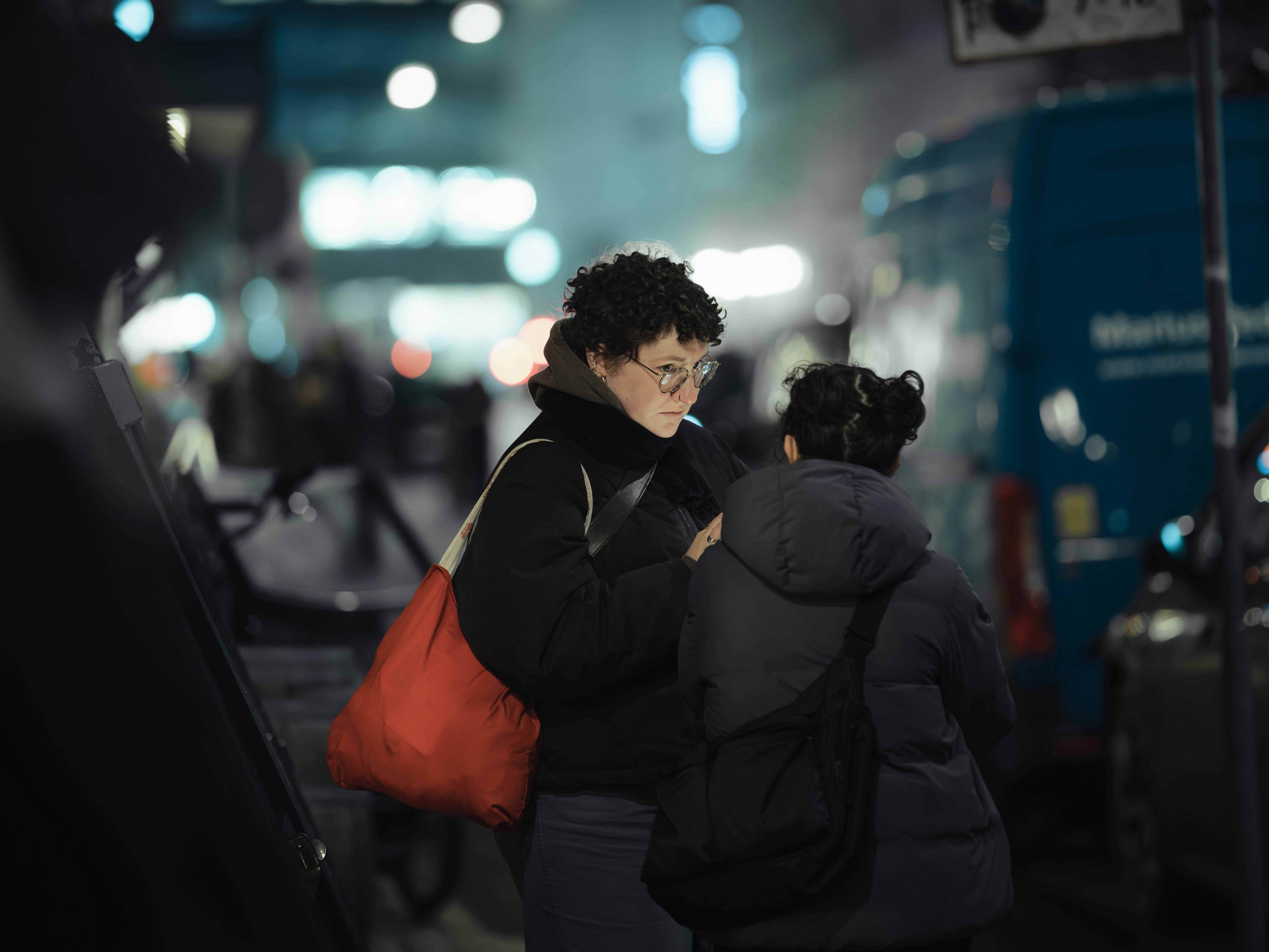 Two people talking on a city street at night.