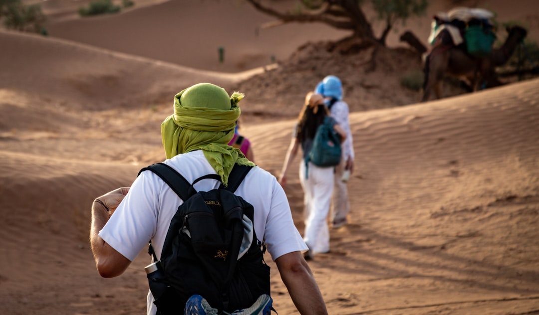 People walking through desert dunes with a camel