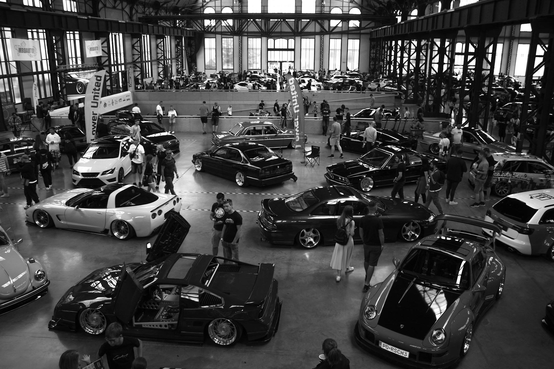 People gathered around custom cars at an indoor exhibition.