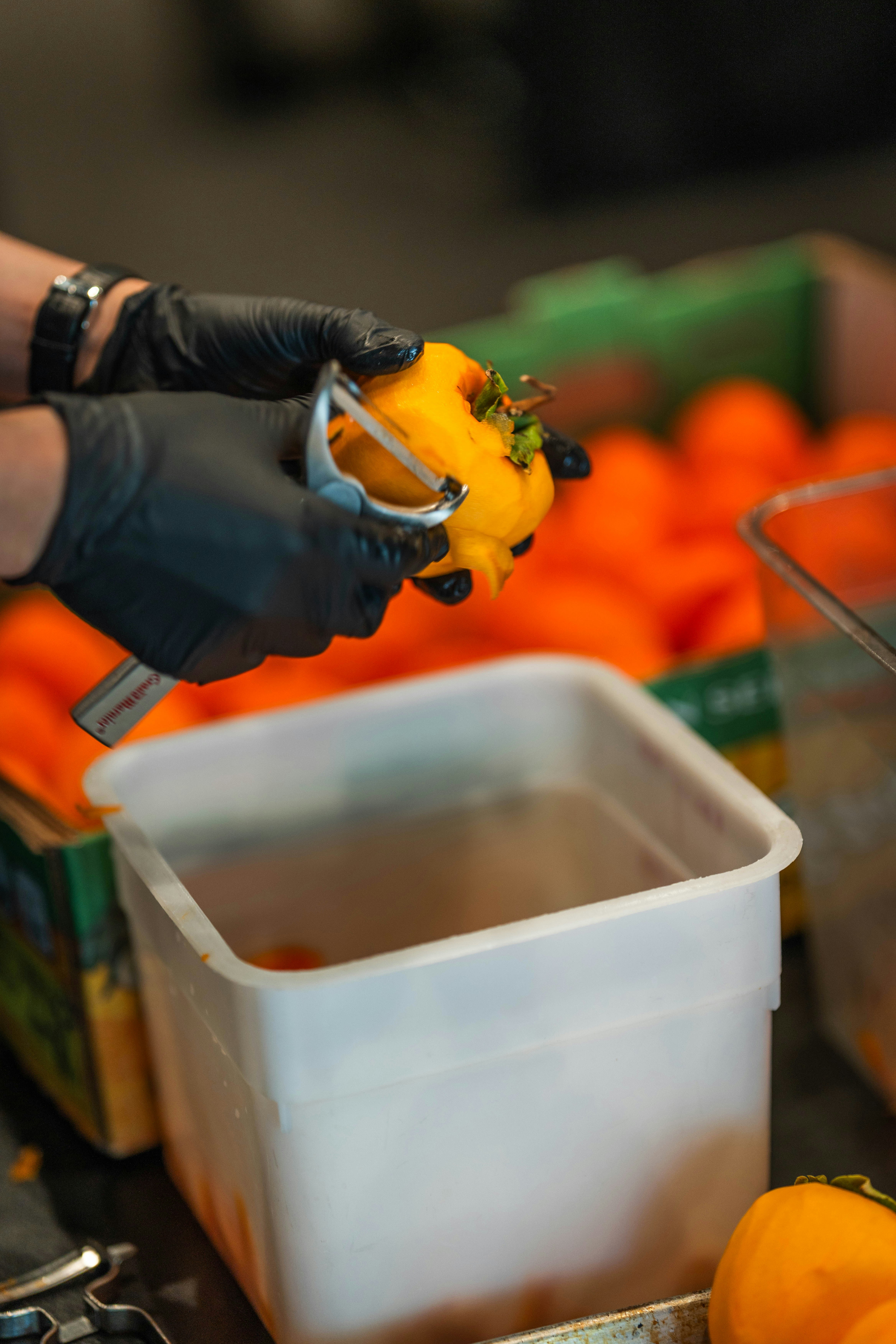 Hands in black gloves peeling a bright orange persimmon.
