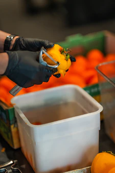 Hands in black gloves peeling a bright orange persimmon.