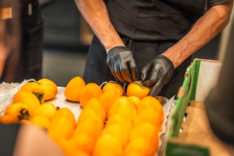Hands in black gloves arranging persimmons on a table.