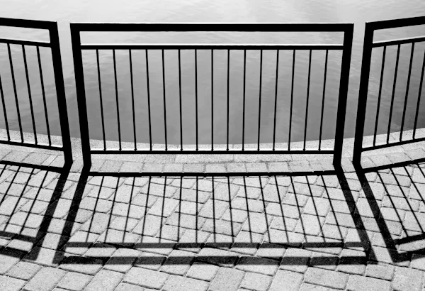 Black metal railing casting shadows on paved ground