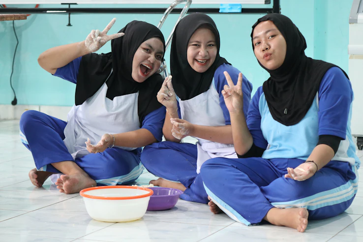 Three smiling women in hijabs making peace signs.