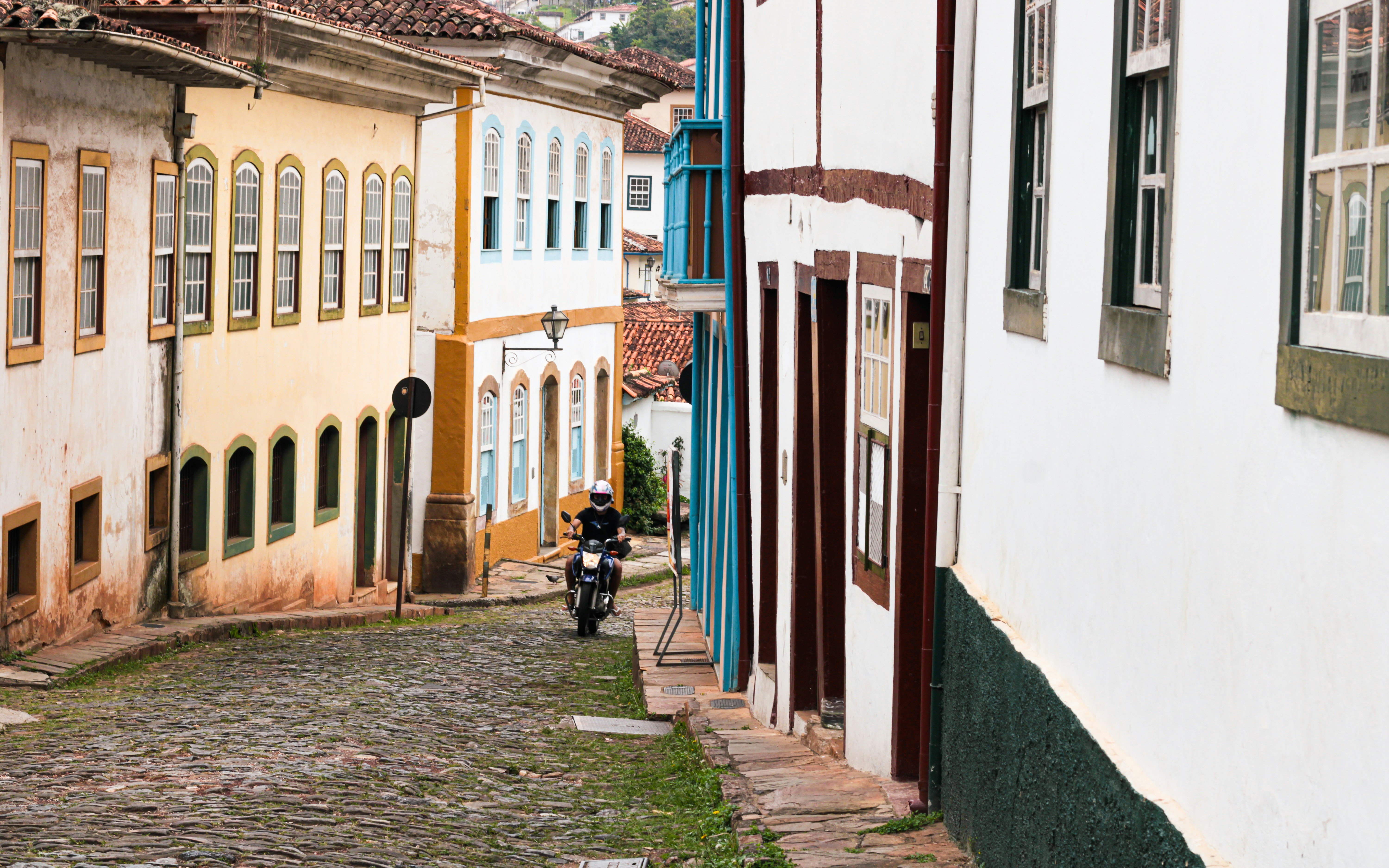 Motorcyclist rides down a cobblestone street lined with colorful buildings.