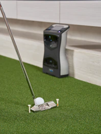 Golf club and ball on artificial turf with device.