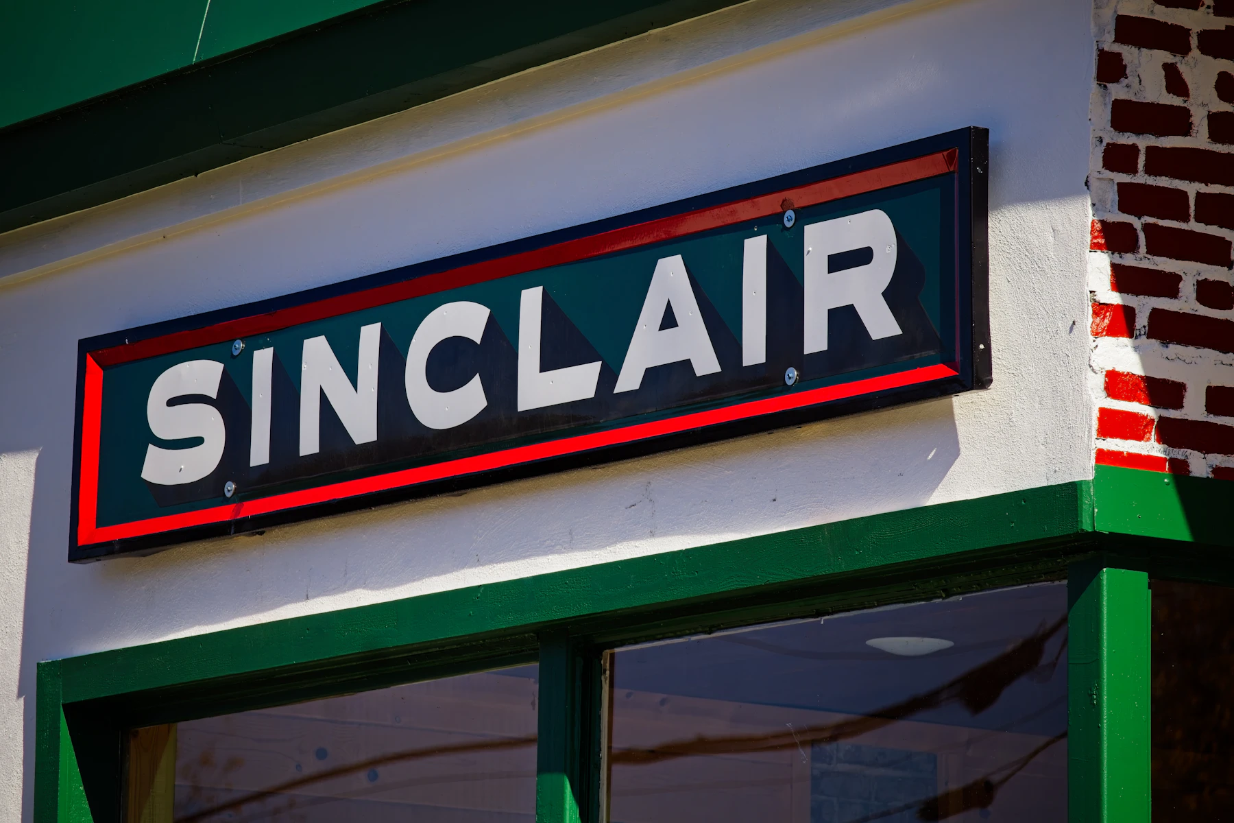 A dark green Sinclair sign with white letters and a red border, screwed to a white wall above a window