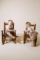 Two babies in overalls sitting on chairs