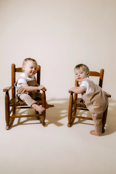 Two babies in overalls sitting on chairs
