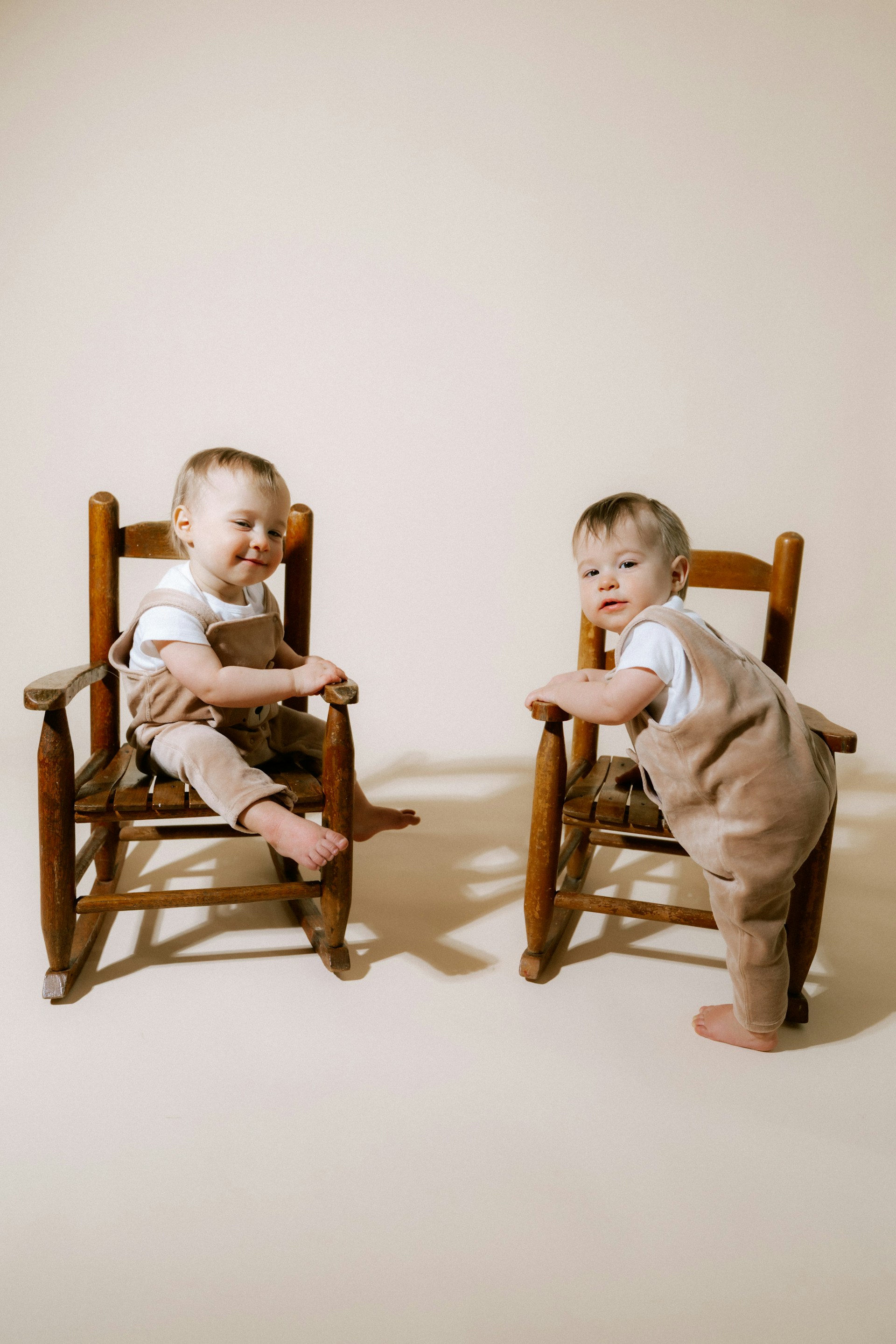 Two babies in overalls sitting on chairs