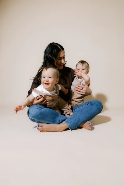 Mother holding two happy babies on neutral background