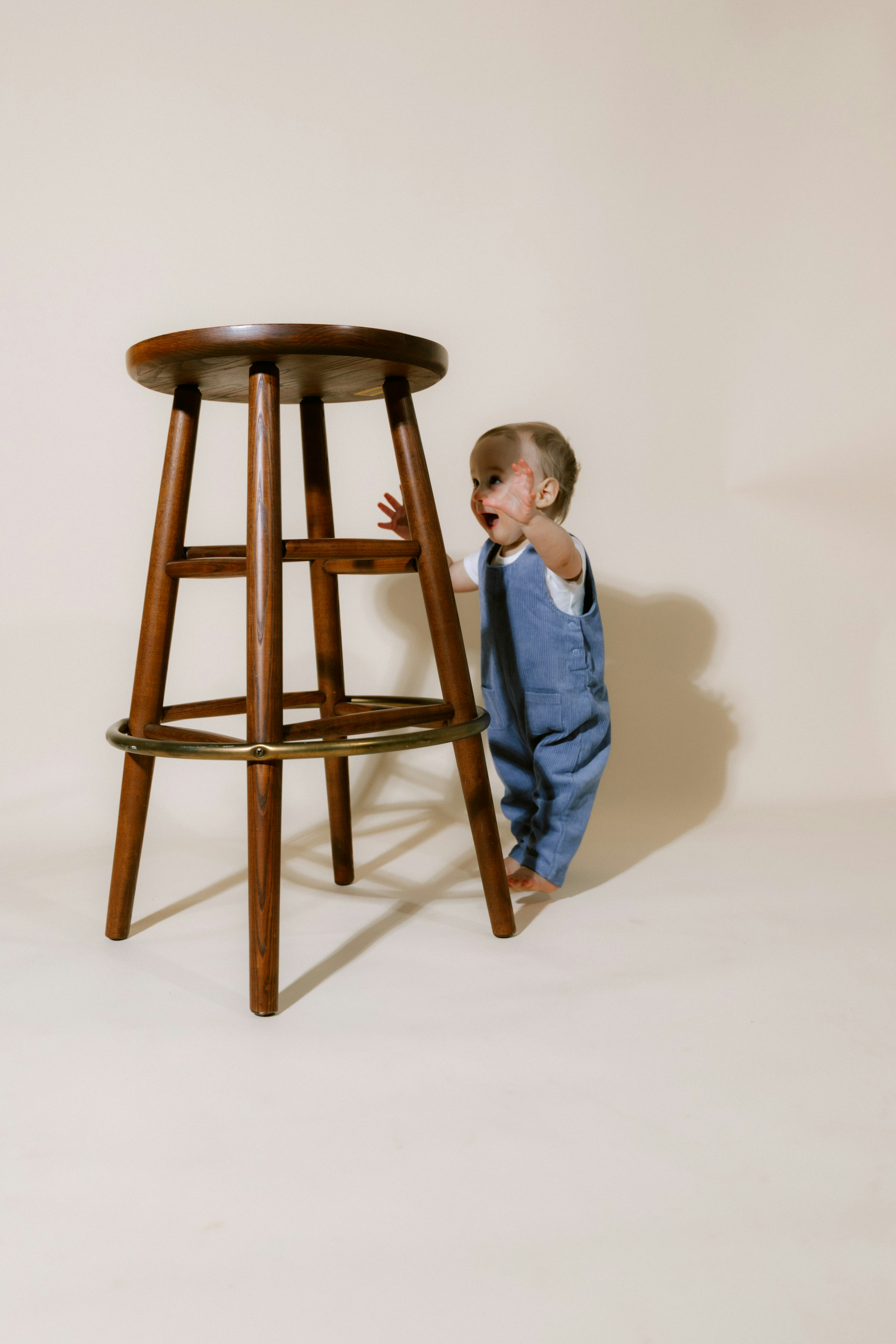 Baby in denim overalls looking at a wooden stool