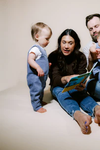 Family reading a book together on a plain background.